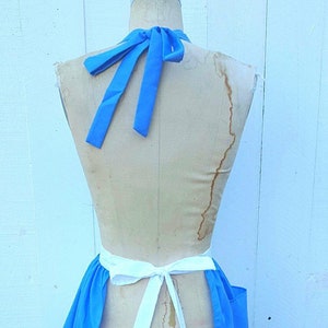 May include: A blue and white apron with a halter neck and a white tie at the waist.