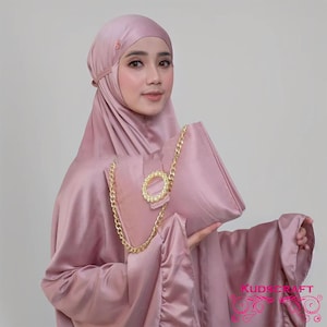 May include: A pink satin headscarf with a gold chain and a decorative gold buckle. The headscarf is worn by a person and is paired with a matching pink satin bag.