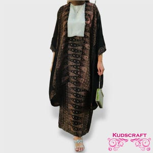 Puede incluir: Un conjunto de top y falda de manga larga con estampado negro y dorado. El top tiene un cuello chal y la falda tiene una cintura alta. El atuendo se complementa con un pequeño bolso verde.