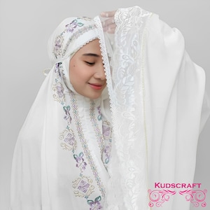 May include: White prayer rug with embroidered floral and geometric designs. The rug has a lace trim and is folded in half. The text "KUDSCRAFT" is visible in the lower right corner of the image.