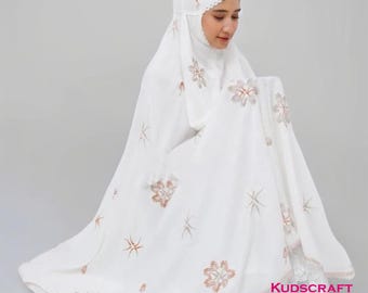 May include: White prayer shawl with delicate lace trim and intricate floral embroidery in shades of brown. The shawl is folded and draped over a person's shoulders. The text "KUDSCRAFT" is visible in the lower right corner of the image.