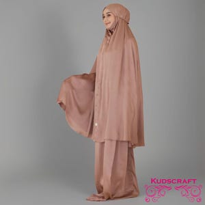 May include: A long, flowing, light brown prayer robe with a matching headscarf. The robe has a loose, comfortable fit and is made of a soft, silky fabric.