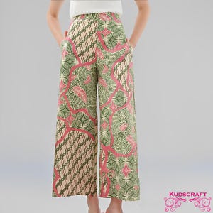 May include: Wide-leg pants with a colorful batik pattern. The pants feature a design with green, pink, and beige hues. The fabric has a floral and geometric pattern. The pants have pockets and a high waist.