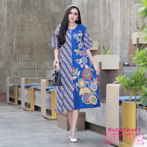 Puede incluir: Un vestido de estampado azul y blanco con un diseño floral en el lado derecho. El vestido tiene mangas cortas y un corte holgado. La modelo lleva tacones blancos.