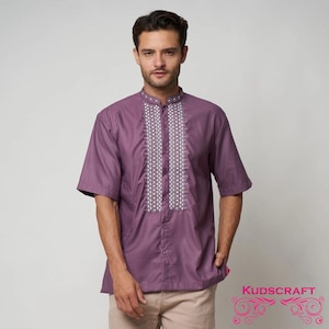 Puede incluir: Una camisa morada de manga corta con cuello mandarín y bordados blancos intrincados en la parte delantera. La camisa tiene cierre de botones y está hecha de tela ligera. La marca "KUDSCRAFT" es visible en la esquina inferior derecha.