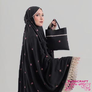 May include: A black prayer garment featuring small pink floral embroidery, a beige lace trim along the edges, and a matching black bag with a beige lace border. The text KUDSCRAFT is visible in the bottom right corner in a pink decorative font.