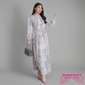 May include: A long-sleeved, gray and white floral print dress with a high neckline and a pleated skirt. The dress has a fitted bodice and a flowy skirt. The model is wearing the dress with a small gray handbag and clear heeled sandals.
