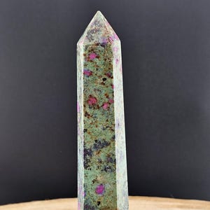 May include: A green and pink ruby in zoisite crystal point. The crystal is faceted and has a pointed tip. The crystal is about 4 inches tall.