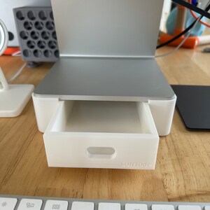 May include: A white desk organizer with a drawer that pulls out. The drawer has a small handle and the word "SUNBODE" printed on the front.