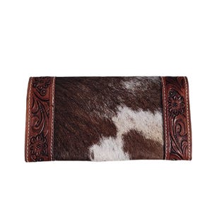 Puede incluir: Una cartera de piel de vaca marr&oacute;n y blanca con un borde de cuero marr&oacute;n con un dise&ntilde;o floral.