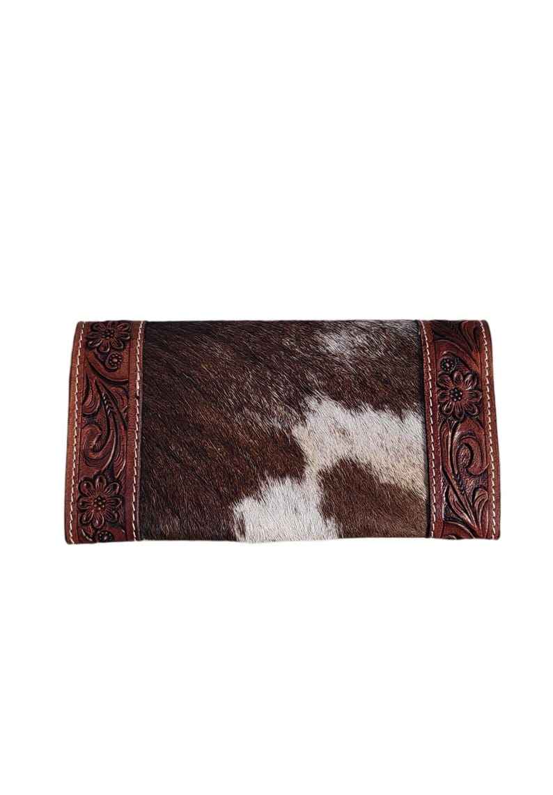 Puede incluir: Una cartera de piel de vaca marr&oacute;n y blanca con un borde de cuero marr&oacute;n con un dise&ntilde;o floral.