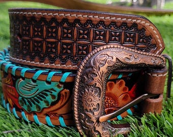May include: A brown leather belt with intricate tooling and a decorative copper buckle. The belt features turquoise accents and a detailed floral design. The top portion of the belt has a geometric pattern.