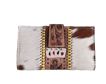 May include: A brown and white cowhide wallet with a yellow stitched border. The front of the wallet features an embossed design of playing cards with four aces and a floral pattern.