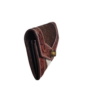 Puede incluir: Una cartera de cuero marr&oacute;n con un dise&ntilde;o estampado blanco y marr&oacute;n. La cartera tiene un cierre a presi&oacute;n y est&aacute; decorada con intrincados bordados florales.