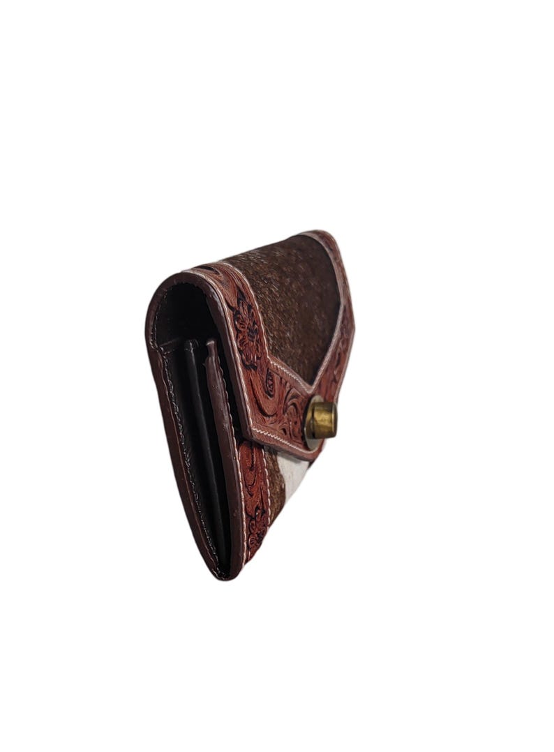 Puede incluir: Una cartera de cuero marr&oacute;n con un dise&ntilde;o estampado blanco y marr&oacute;n. La cartera tiene un cierre a presi&oacute;n y est&aacute; decorada con intrincados bordados florales.