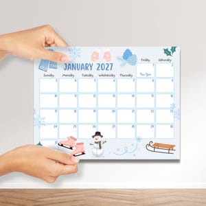 May include: A light blue January 2027 calendar with winter illustrations. The calendar features images of ice skates, mittens, snowflakes, and a snowman. The calendar is held by two hands.