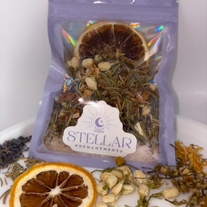 Può includere: Un sacchetto trasparente pieno di erbe essiccate, fiori e una fetta di arancia essiccata. Il sacchetto ha un effetto olografico e un'etichetta con la scritta "STELLAR ENCHANTMENTS". Erbe essiccate e fette di arancia sciolte sono disposte intorno al sacchetto.