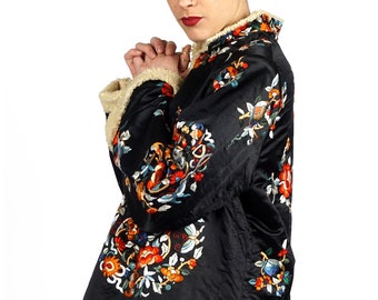 May include: A black satin jacket with a white fur trim and colorful floral embroidery. The jacket has a mandarin collar and a long sleeve.