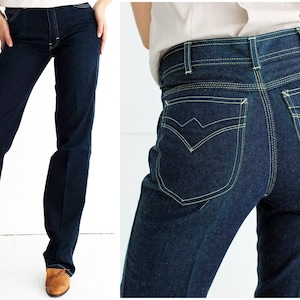 May include: A pair of dark blue denim jeans with a high waist and a straight leg. The jeans have a yellow topstitching detail and a small red label with the text "LA VIE" on the back right pocket.