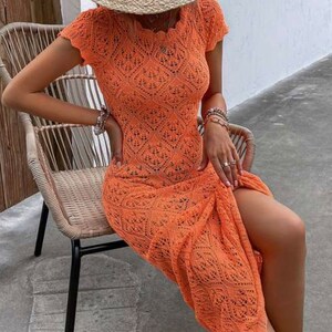 May include: A long, orange crochet dress with a side slit and short sleeves. The dress is made of a delicate, open-weave fabric.