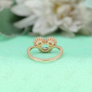 May include: A gold ring with a large round center stone surrounded by smaller stones. The ring is set with two heart-shaped halos of smaller stones.