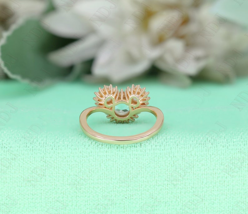 May include: A gold ring with a large round center stone surrounded by smaller stones. The ring is set with two heart-shaped halos of smaller stones.