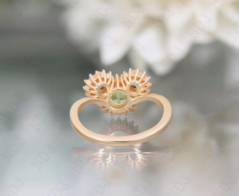 Op de afbeelding: Een gouden ring met een groene edelsteen omringd door kleinere diamanten. De ring is in de vorm van een hart gezet.