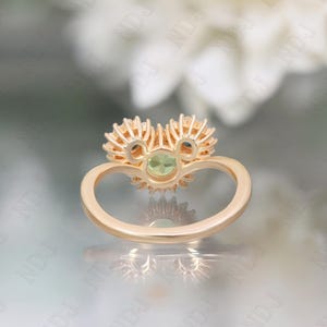 Op de afbeelding: Een gouden ring met een groene edelsteen omringd door kleinere diamanten. De ring is in de vorm van een hart gezet.