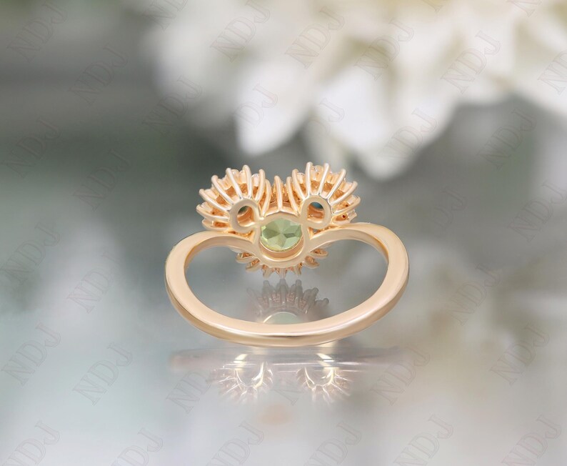 Op de afbeelding: Een gouden ring met een groene edelsteen omringd door kleinere diamanten. De ring is in de vorm van een hart gezet.