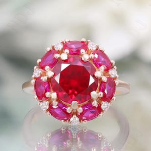 May include: A red ruby ring with a large center stone surrounded by smaller rubies and diamonds. The ring is set in gold.