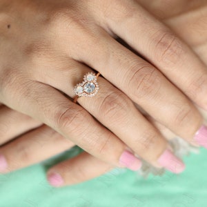 May include: A heart-shaped ring with a large, clear gemstone surrounded by smaller, clear gemstones. The ring is set in rose gold.