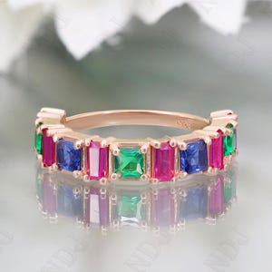 May include: A rose gold band ring featuring a row of colourful square-shaped gemstones. The gemstones are red, green and blue.