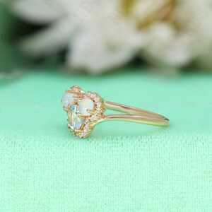 May include: A delicate gold ring with three oval-shaped gemstones. The center stone is a light blue aquamarine, flanked by two white opals. The ring is set with small diamonds around the stones.