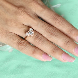 May include: A heart-shaped ring with a large, clear center stone surrounded by smaller, clear stones. The ring is set in rose gold and is worn on a hand with pink nail polish.