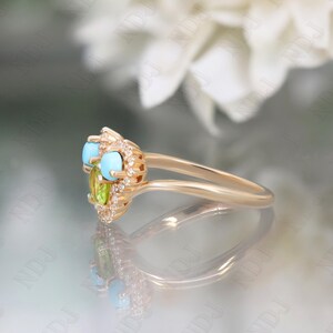 Op de afbeelding: Een gouden ring met een hartvormige zetting met turquoise en groene edelstenen, omringd door kleine diamanten.