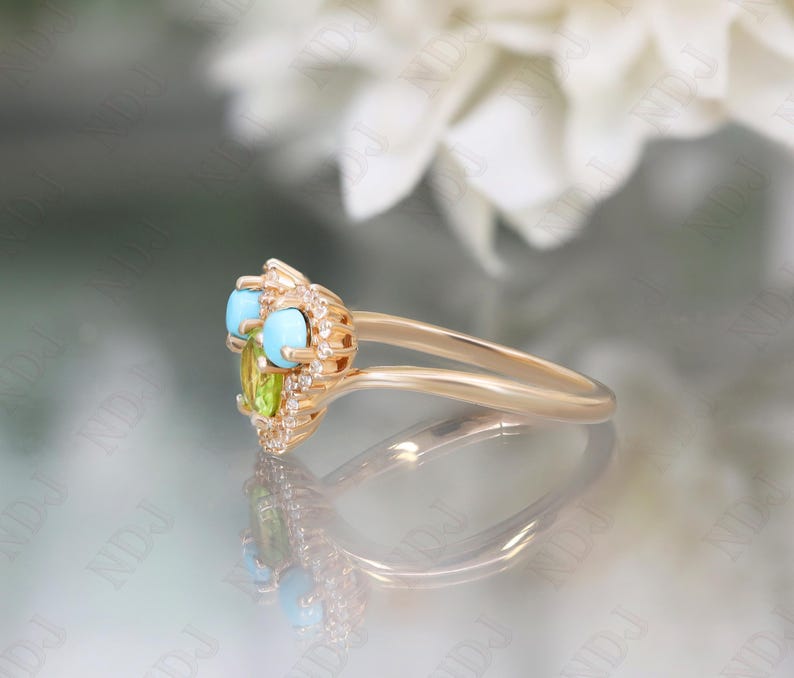 Op de afbeelding: Een gouden ring met een hartvormige zetting met turquoise en groene edelstenen, omringd door kleine diamanten.