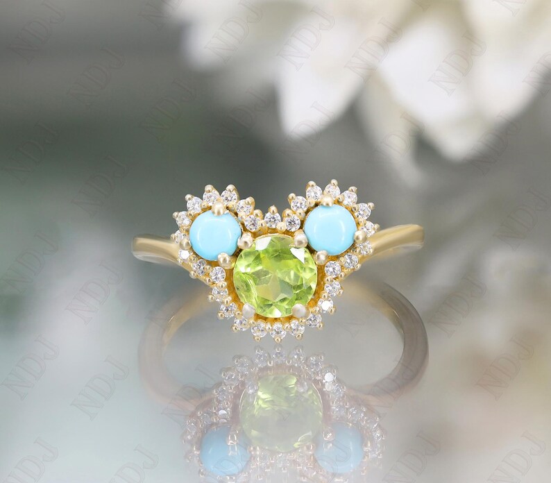 Op de afbeelding: Een gouden ring met een groene peridoot edelsteen omringd door kleine diamanten. De ring heeft ook twee turquoise edelstenen, elk omringd door kleine diamanten.