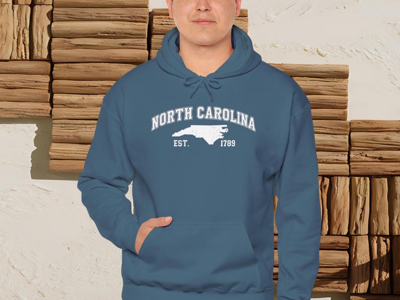 May include: A teal hoodie with a front pocket and a drawstring hood. The front of the hoodie features the words "North Carolina" in a curved font, with a white outline of the state and the text "Est. 1789" below it.