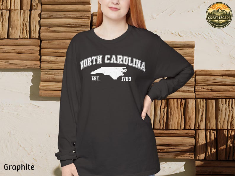 May include: Graphite long-sleeve shirt featuring the text "North Carolina" above a white outline of the state and the text "Est. 1789". The shirt has a crew neck and is made of a soft material.