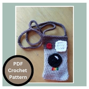 May include: A crochet pattern for a small camera-shaped bag with a strap. The bag is gray with a black lens, red and white accents, and a rainbow stripe. The pattern is available as a PDF download.