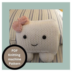 May include: A white knitted plush toy shaped like a rectangle with a pink bow on top. The toy has a smiling face with black eyes and a black mouth. The toy is sitting on a striped blue and white fabric.