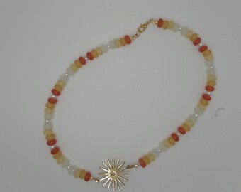 May include: A beaded necklace featuring a gold sunburst pendant. The necklace is composed of small, round beads in shades of orange, yellow, and white. The clasp and sunburst pendant are gold-colored.