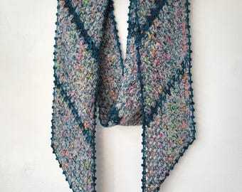 May include: A hand-knitted scarf in a mix of colours, including pink, blue, and green, with a textured pattern and teal edging. The scarf is displayed on a wooden hanger. The scarf measures approximately 150 cm in length.
