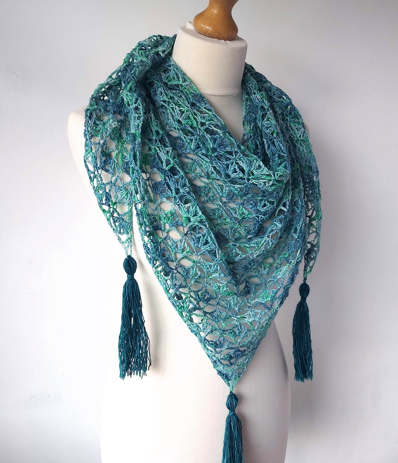 May include: A teal and green crocheted shawl with a triangular shape and fringe tassels.