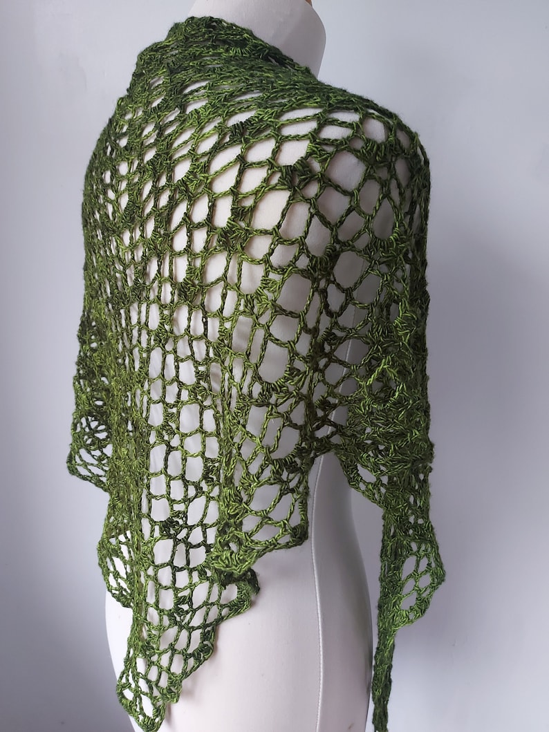 May include: A green crochet shawl with a delicate openwork pattern. The shawl is draped over a white dress form.