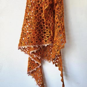 Op de afbeelding: Een gehaakte sjaal in tinten oranje en roze. De sjaal heeft een delicate kantzoom en is gemaakt van een fijn garen.