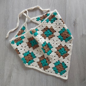 Peut inclure: Une écharpe en crochet blanche avec des carrés marrons et turquoise. L'écharpe a une longue sangle fine qui peut être nouée autour du cou.