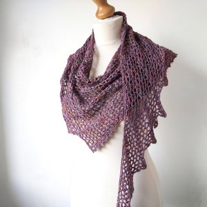 Puede incluir: Un chal de ganchillo morado y marr&oacute;n con un dise&ntilde;o de encaje. El chal est&aacute; drapeado sobre un maniqu&iacute; blanco.