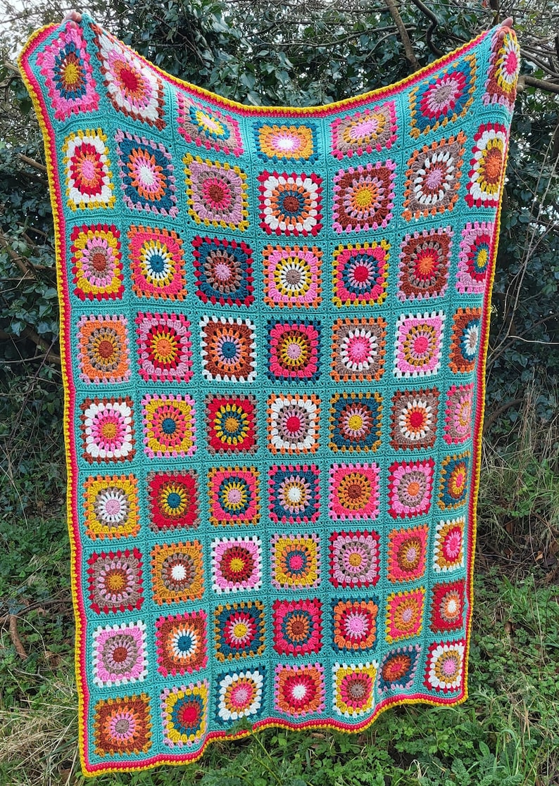 May include: A vibrant, hand-crocheted blanket. It has a turquoise base with many square patterns in pink, yellow, orange, and brown. The blanket is edged with a yellow border and a red trim.