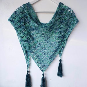 May include: A teal and green crocheted shawl with a triangular shape and fringe tassels.